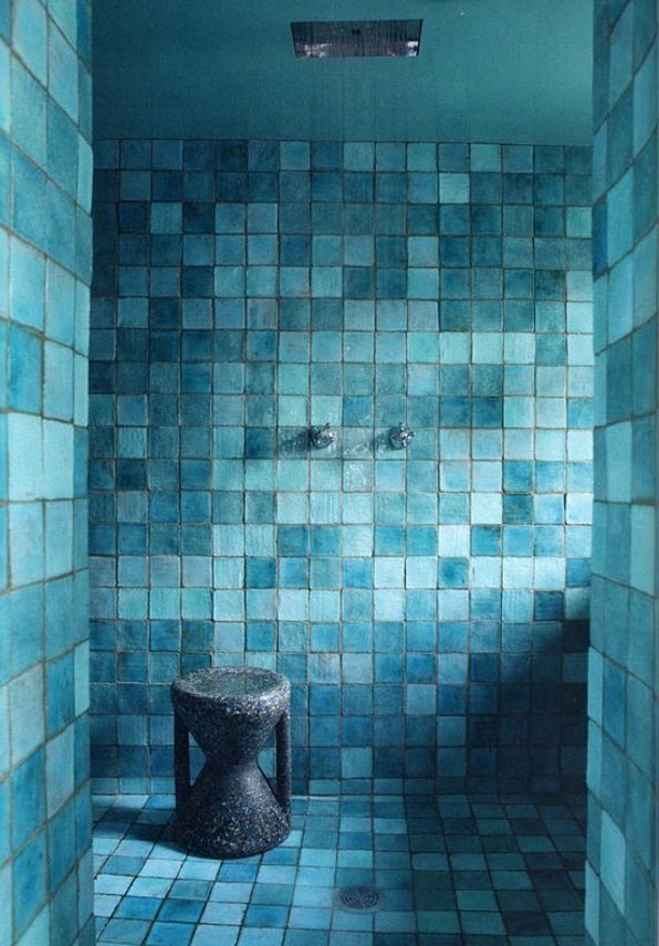 a blue tiled room with a stool in the corner and tile on the wall behind it