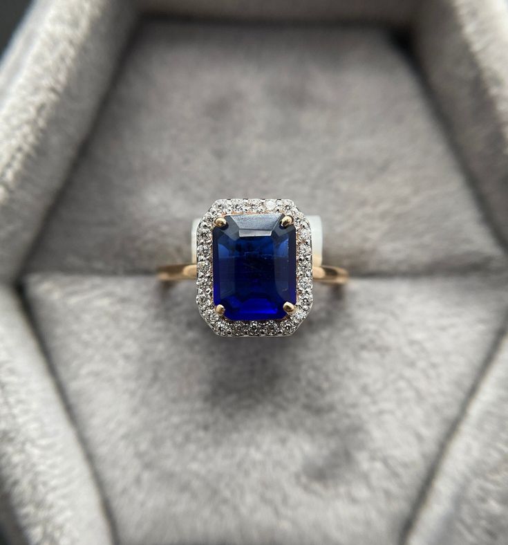 an engagement ring with a blue stone surrounded by white and yellow diamonds in a velvet box