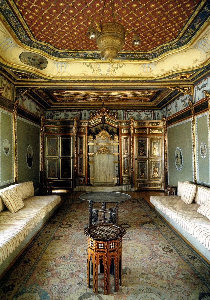 a room with couches, tables and mirrors on the walls is decorated in gold