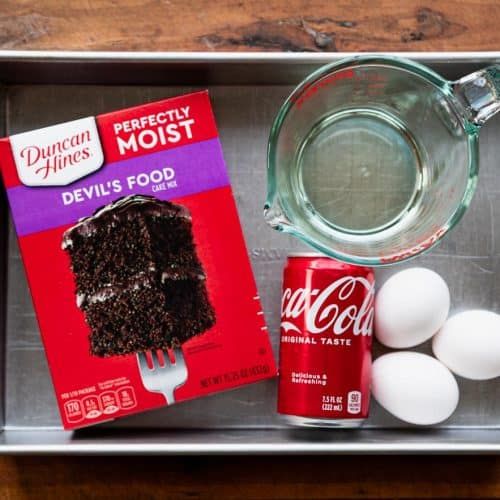 ingredients to make chocolate cake laid out on a baking sheet in a metal pan, including eggs and milk