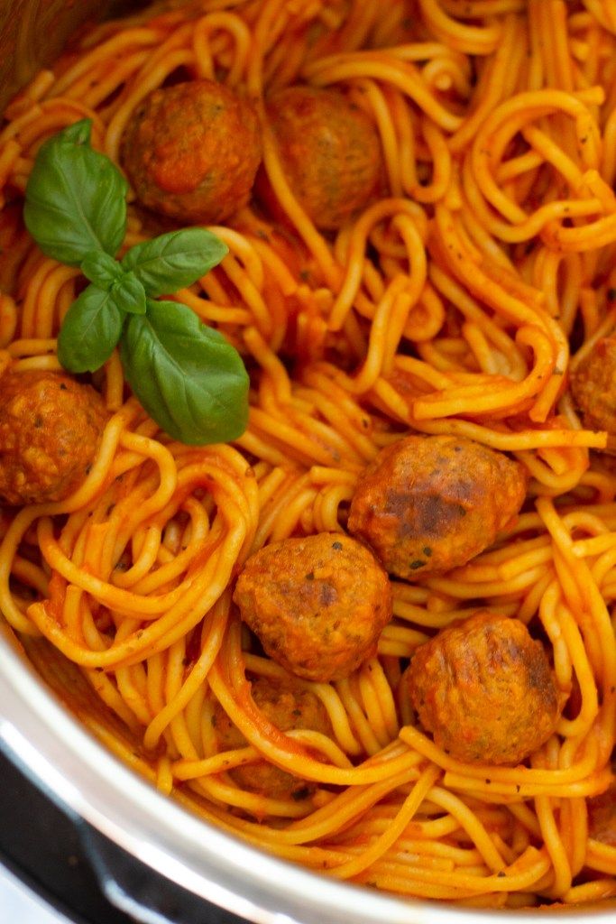 spaghetti with meatballs and basil leaves in an instant pot on the stove top, ready to be cooked