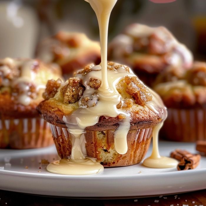 a person pouring icing onto some cupcakes on a plate with other muffins in the background