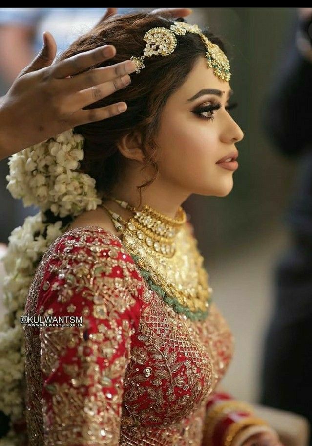 a woman in a red and gold bridal outfit getting her hair combed by someone's hand