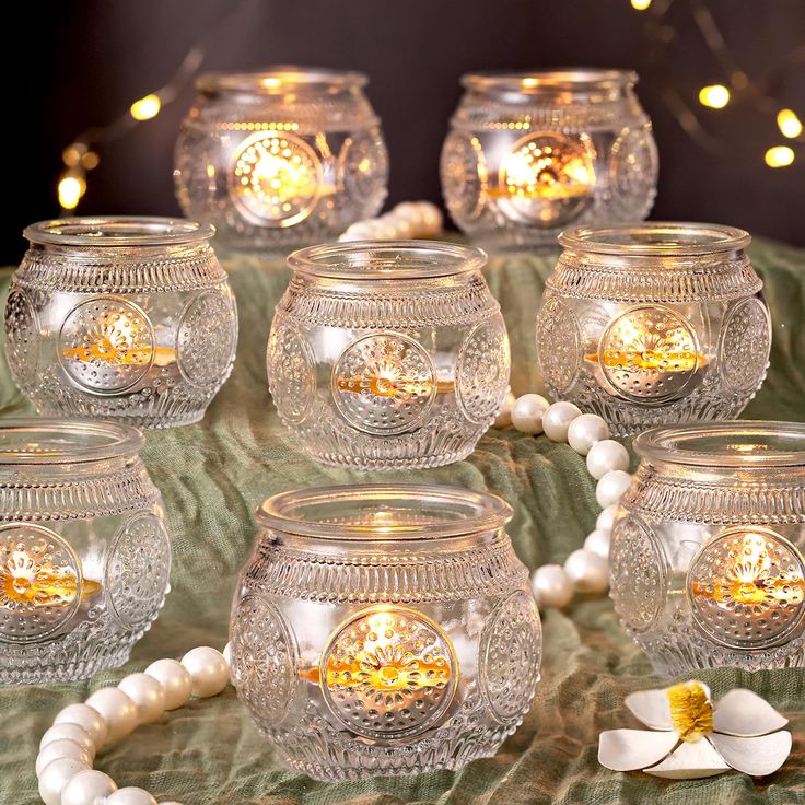 there are many glass jars with lights in them on the table next to pearls and beads