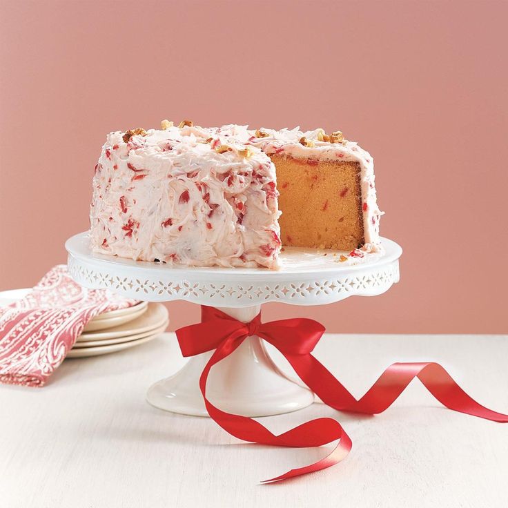 a white cake on a plate with a red ribbon around it and a slice missing