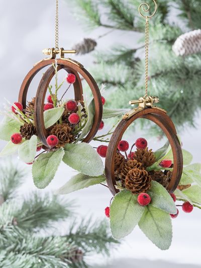 two wooden hoop ornaments hanging from a christmas tree with pine cones and berries on them