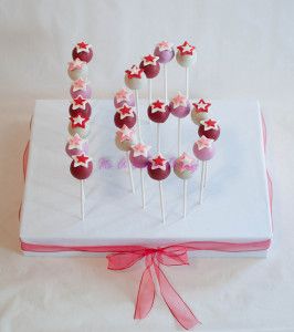 the cake pops are decorated with stars and pink ribbons on top of a white box