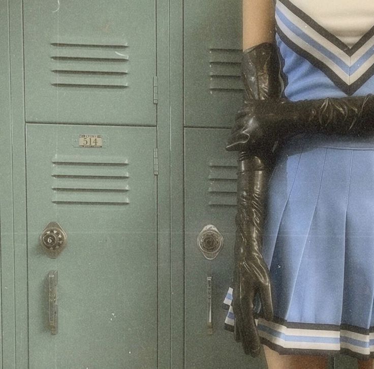 a woman in a blue dress and black gloves standing next to lockers with her hands on her hips