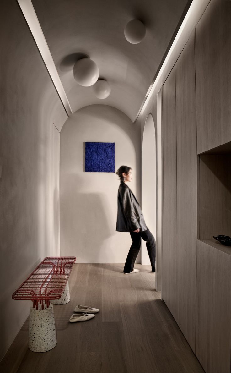 a woman walking down a hallway next to a red bench and white wall with blue artwork on it