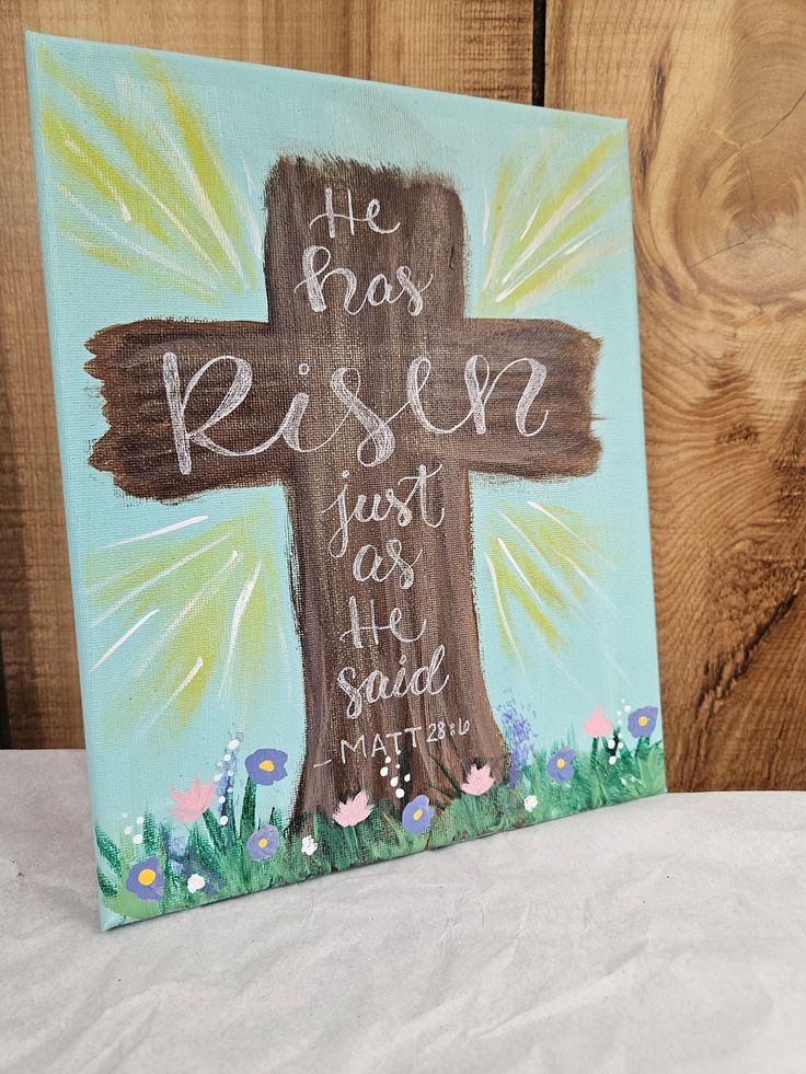 a wooden cross painted with the words he has risen just as he said