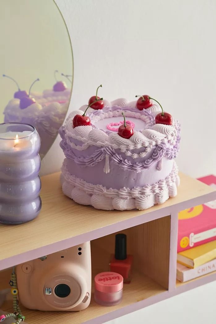 a cake with cherries on it sitting on a shelf next to a mirror and camera