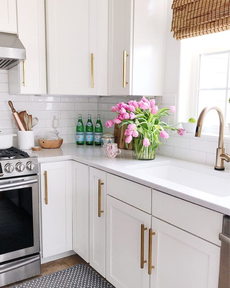 a kitchen with white cabinets and pink flowers in a vase on the counter top next to an oven