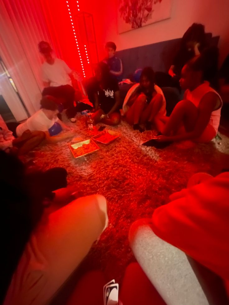 a group of people sitting on the floor in a room with red light coming from behind them