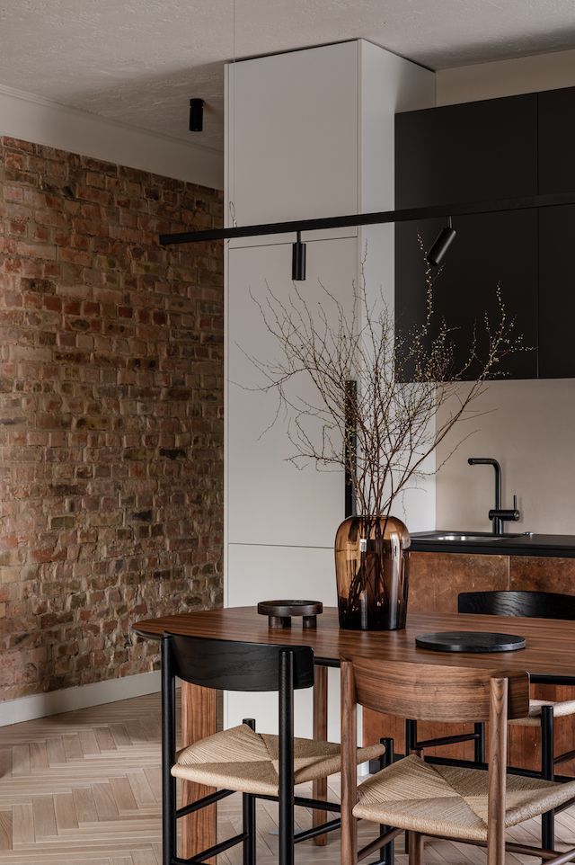 a kitchen table with chairs and a vase on it in front of a brick wall