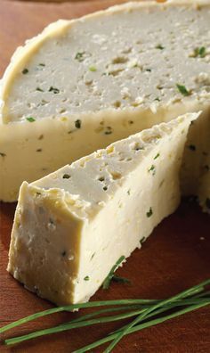 a piece of cheese sitting on top of a cutting board next to some green herbs