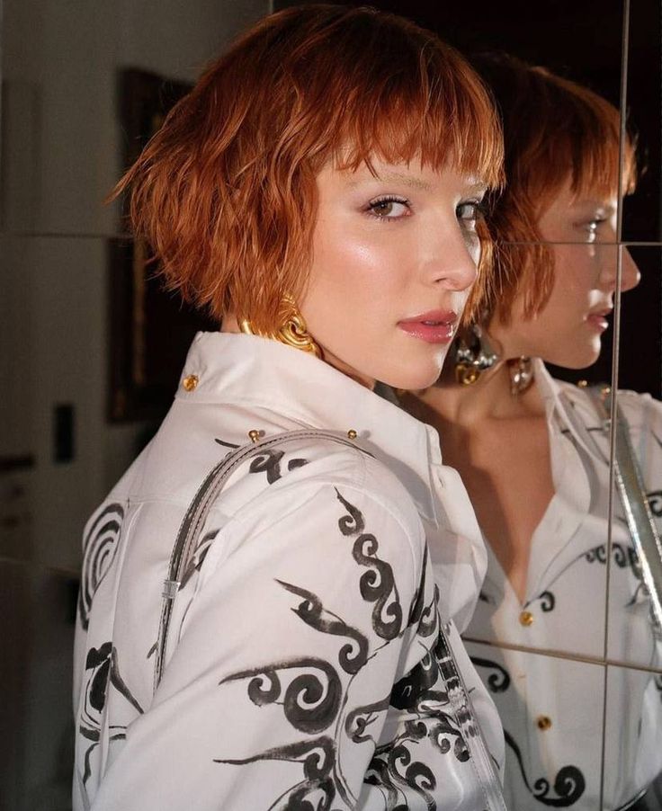 two women with short red hair are looking at themselves in the mirror and one is wearing gold earrings