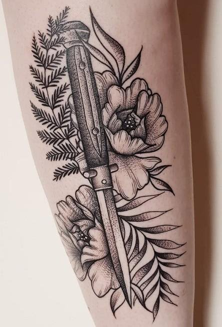 a black and white image of a knife with flowers on the side of a woman's leg