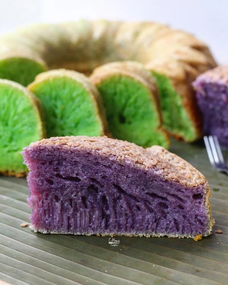 a purple and green cake sitting on top of a wooden table next to a fork