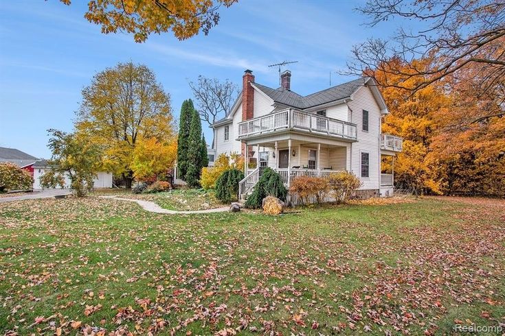 a large white house sitting on top of a lush green field covered in fall leaves