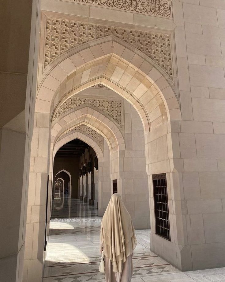 a person standing under an archway in the middle of a building with white walls and arches