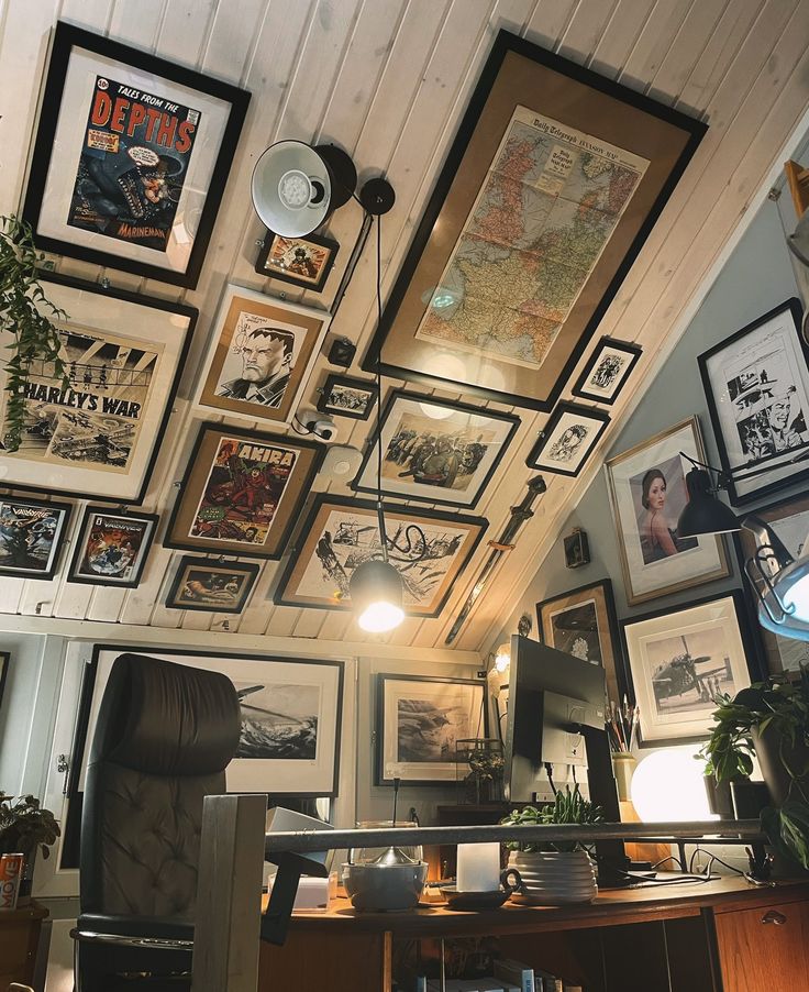 a room filled with lots of framed pictures on the wall above a desk and chair