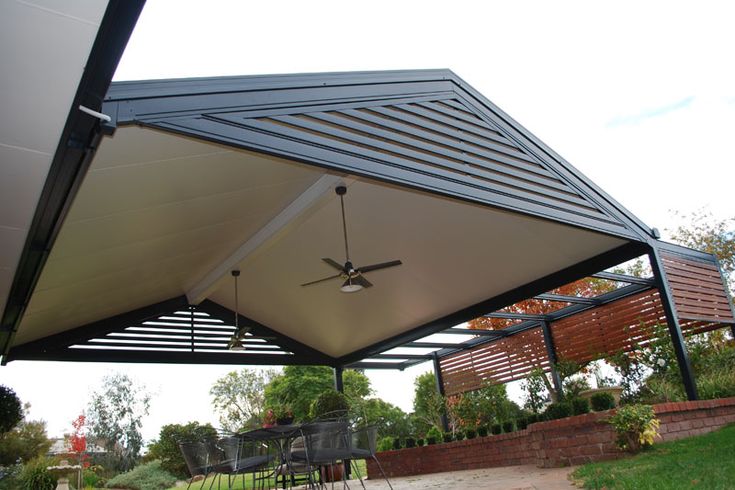 an outdoor covered patio with ceiling fans in the center and on the other side is a garden area