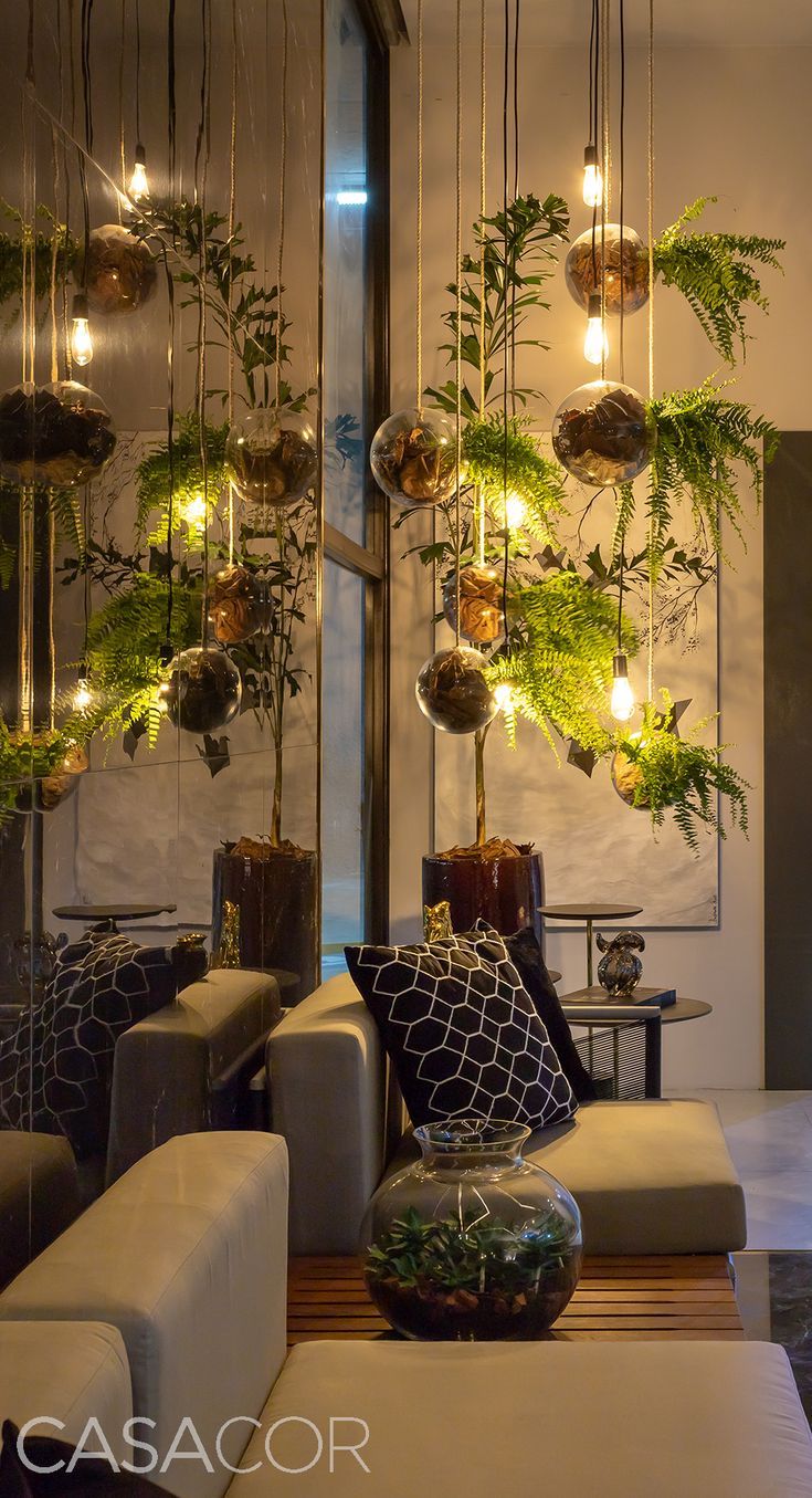 a living room filled with lots of furniture and plants hanging from the ceiling above them