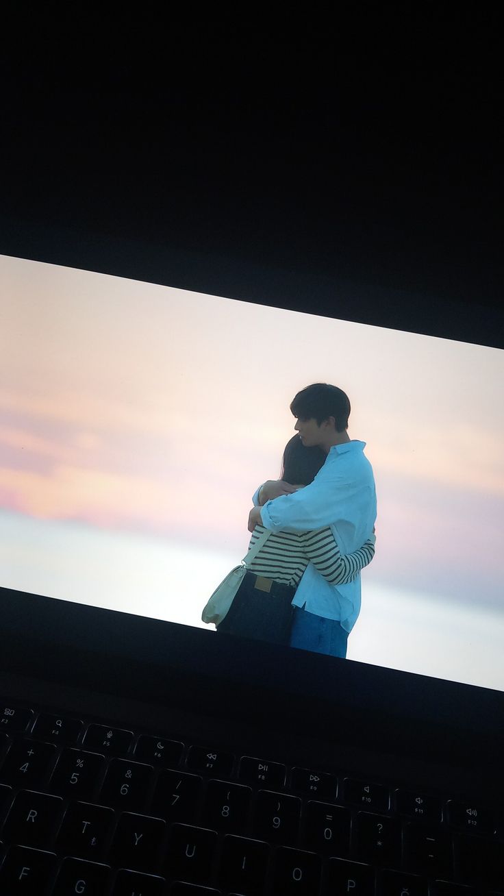 a man and woman embracing each other in front of a large screen with the sky behind them