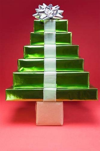 a green christmas tree shaped gift box with white ribbon and silver bow on pink background