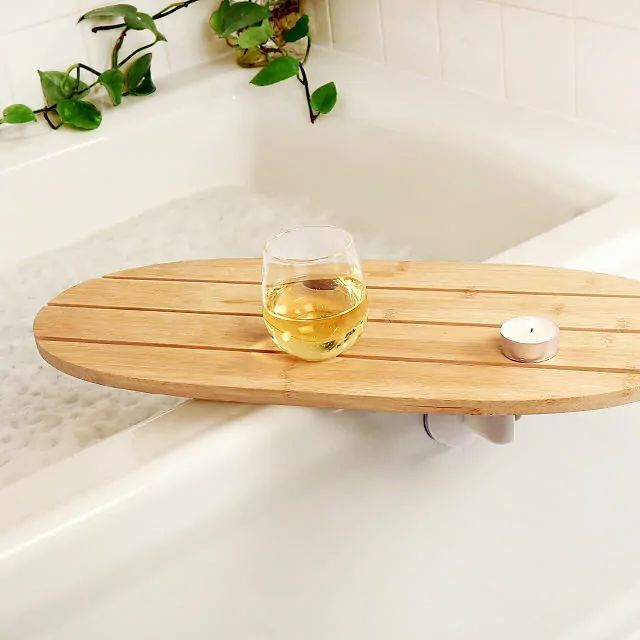 a glass of wine sitting on top of a bath tub next to a wooden tray