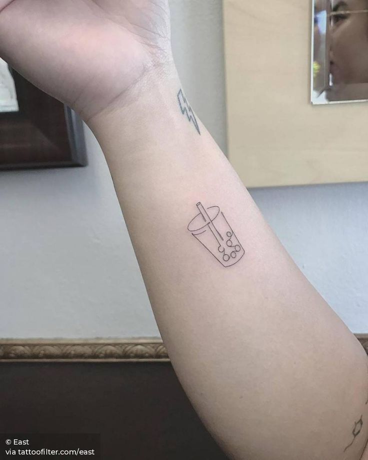 a person's arm with a tattoo on it and a drink in the cup