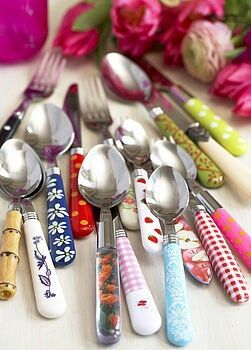 there are many spoons and forks on the table with flowers in the back ground