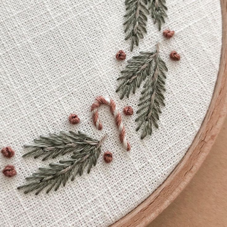 a close up of a cross stitch pattern on a wooden hoop with candy canes and pine cones