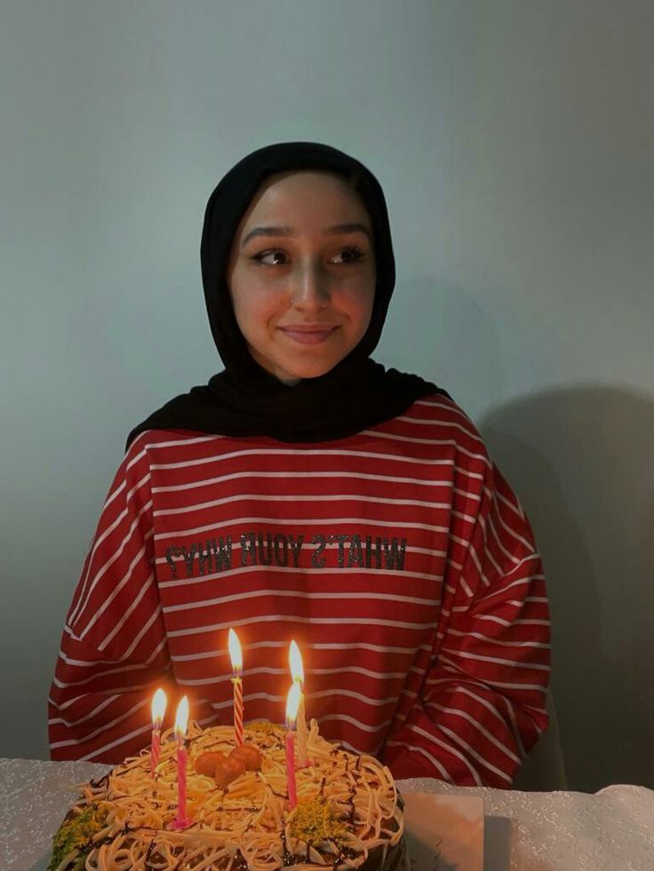 a young woman sitting in front of a cake with lit candles on top of it