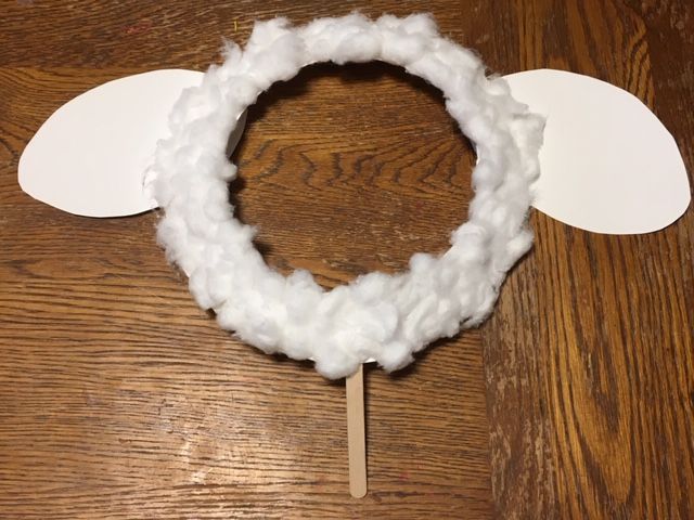 a white yarn wreath on a wooden table with two paper circles attached to the front