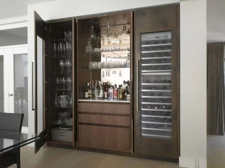 a bar with wine glasses and bottles on the shelves in front of it, next to a dining room table