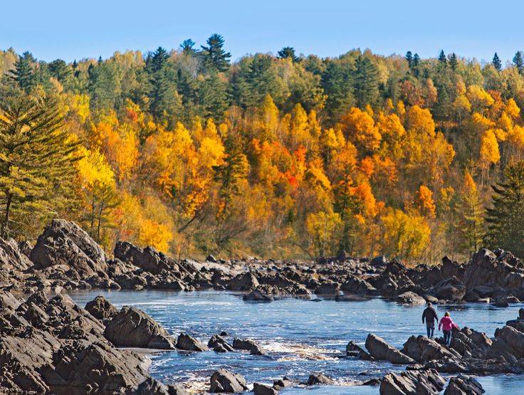 two people standing on rocks in the middle of a river surrounded by fall colored trees