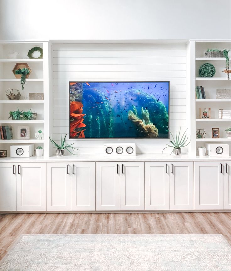 a living room with white bookcases and an aquarium on the wall above it