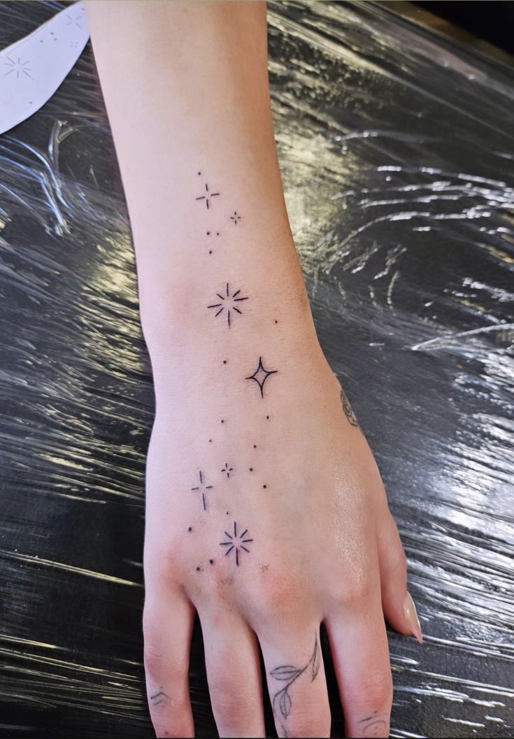 a woman's hand with tattoos on it and stars in the sky above her