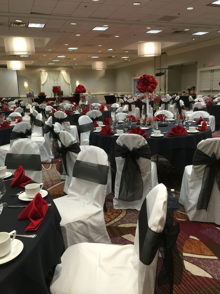 the banquet room is set up with black and white linens, red rose centerpieces, and silver napkins