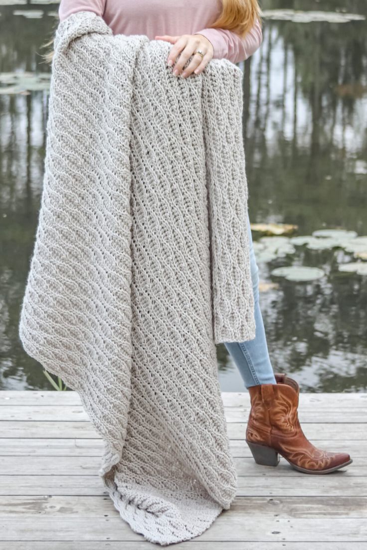 a woman standing on a dock holding up a blanket