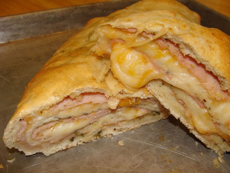 a sandwich cut in half sitting on top of a metal pan covered in cheese and ham