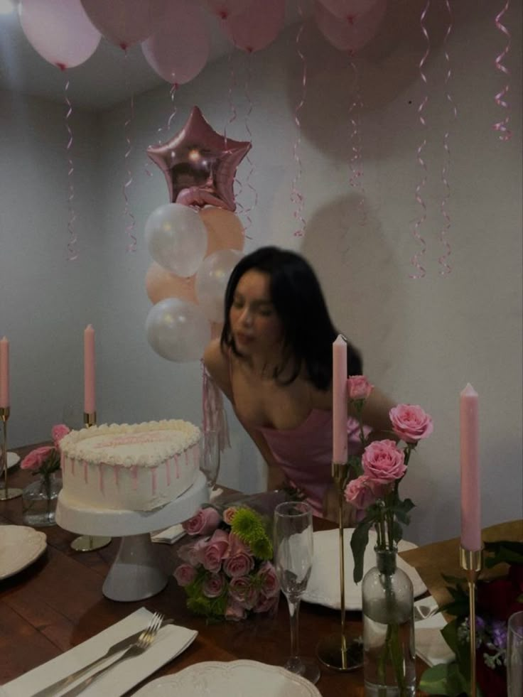 a woman sitting at a table in front of a cake with pink flowers and balloons