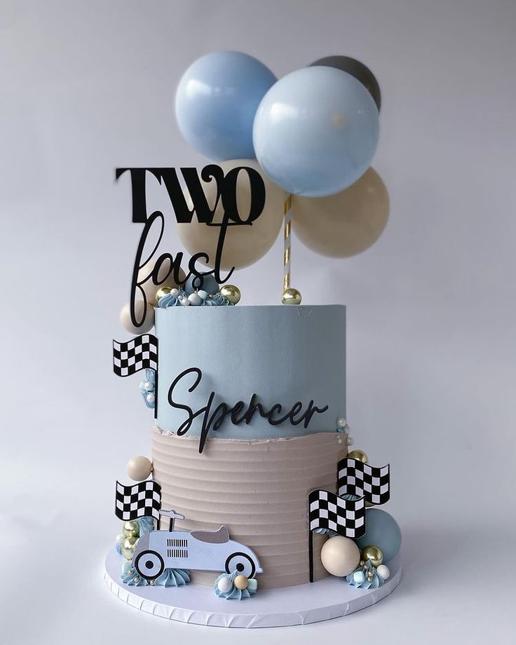 a two tiered cake with blue and white balloons in the shape of race cars