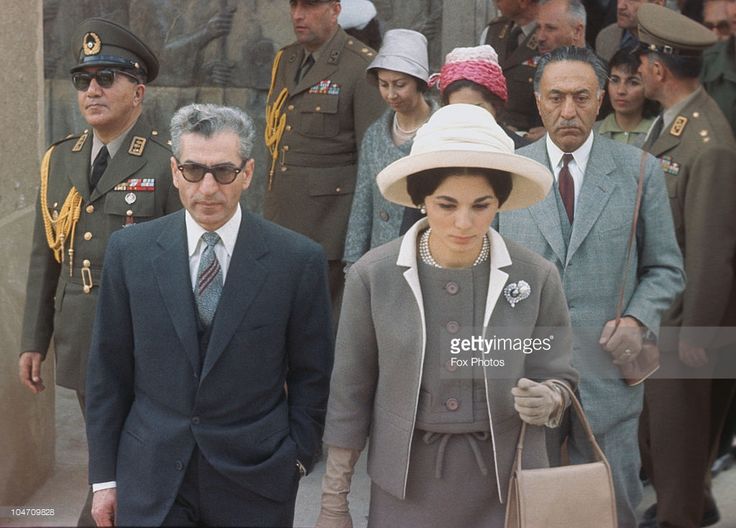 a woman in a gray dress and hat walking next to a man in a suit