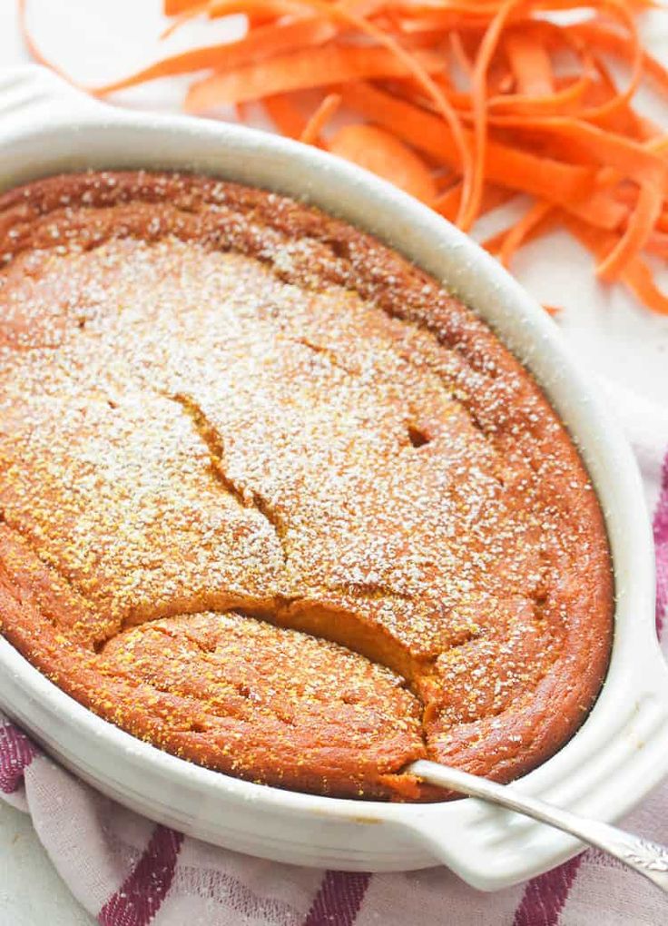 carrot cake with powdered sugar on top and sliced carrots in the back ground