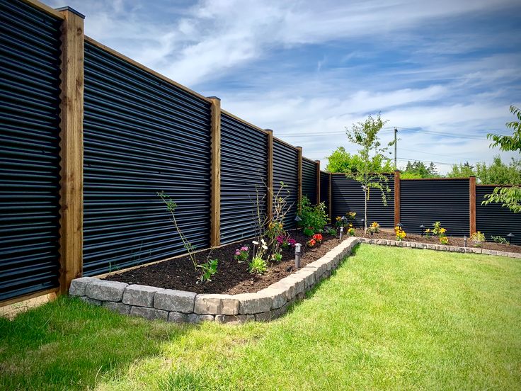 a garden area with grass and flowers in the foreground, next to a black fence