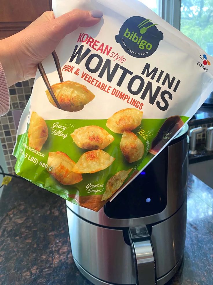 someone is holding up a bag of wontons in front of an air fryer