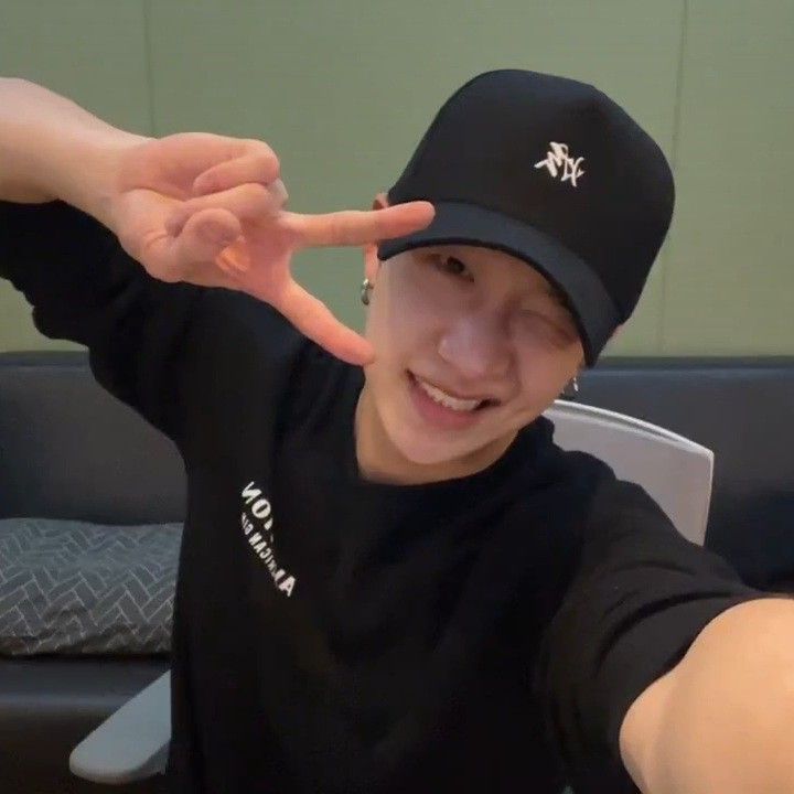 a young man wearing a black hat and making the peace sign with his hand while sitting at a table