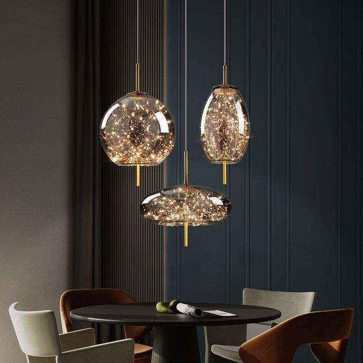 three lights hanging over a table in a room with chairs and a lamp on the wall